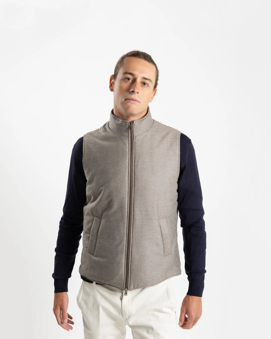 A refined take on the classic gilet, this sleeveless vest is crafted from a premium wool-blend fabric in a warm greige melange. Subtly padded for lightweight insulation without bulk, it layers effortlessly over knitwear or a collared shirt for a polished smart-casual look.

Featuring a stand collar, full-length zip fastening with a gunmetal pull, and clean jetted front pockets, the cut is slim and tailored — designed to sit neatly under a jacket or wear alone as an outer layer.