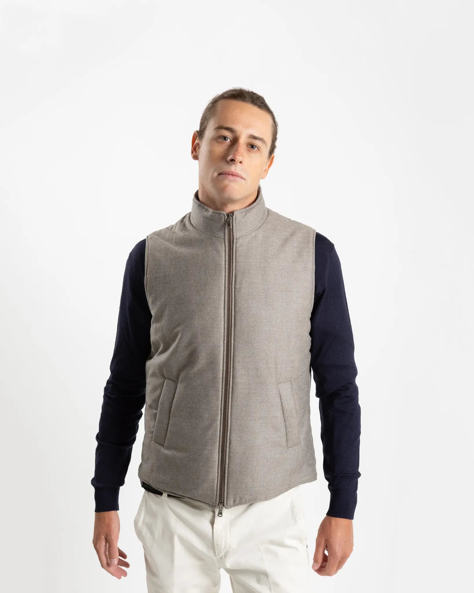 A refined take on the classic gilet, this sleeveless vest is crafted from a premium wool-blend fabric in a warm greige melange. Subtly padded for lightweight insulation without bulk, it layers effortlessly over knitwear or a collared shirt for a polished smart-casual look.

Featuring a stand collar, full-length zip fastening with a gunmetal pull, and clean jetted front pockets, the cut is slim and tailored — designed to sit neatly under a jacket or wear alone as an outer layer.