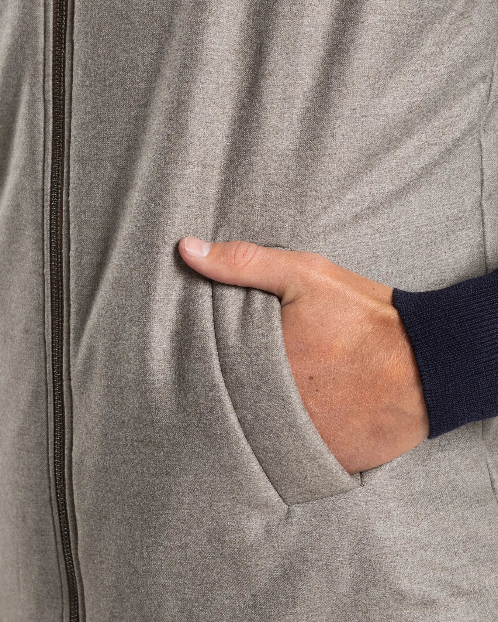 A refined take on the classic gilet, this sleeveless vest is crafted from a premium wool-blend fabric in a warm greige melange. Subtly padded for lightweight insulation without bulk, it layers effortlessly over knitwear or a collared shirt for a polished smart-casual look.

Featuring a stand collar, full-length zip fastening with a gunmetal pull, and clean jetted front pockets, the cut is slim and tailored — designed to sit neatly under a jacket or wear alone as an outer layer.