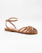 Shop the CIRA5 flat lattice sandal in tan calf leather. Italian-made with a woven strap detail, adjustable ankle strap, and rubber sole. Understated summer elegance.