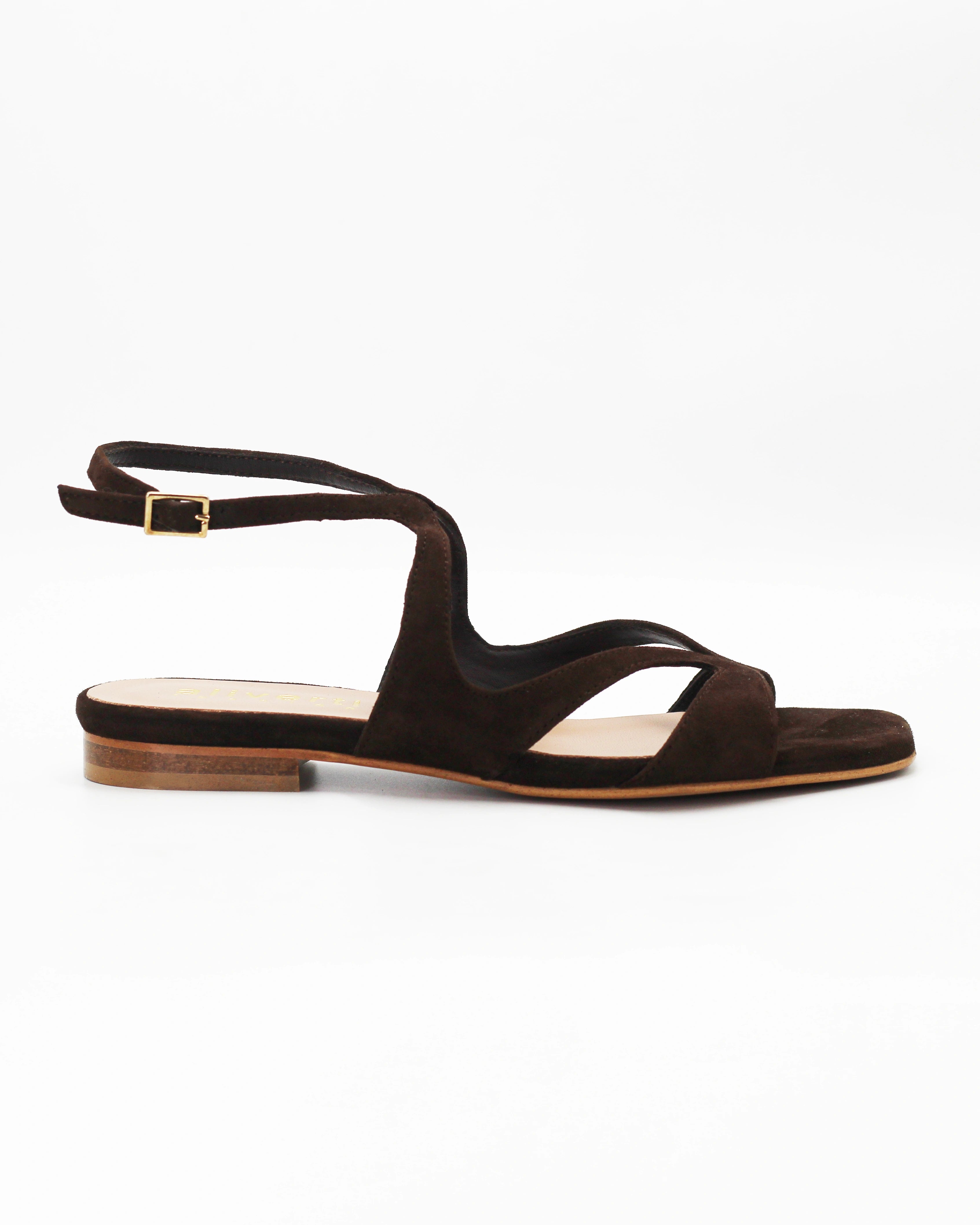 PATTY20 flat sandal in testa di moro suede with a sleek asymmetric toe strap and adjustable ankle strap. Handcrafted in Italy. Understated and easy.