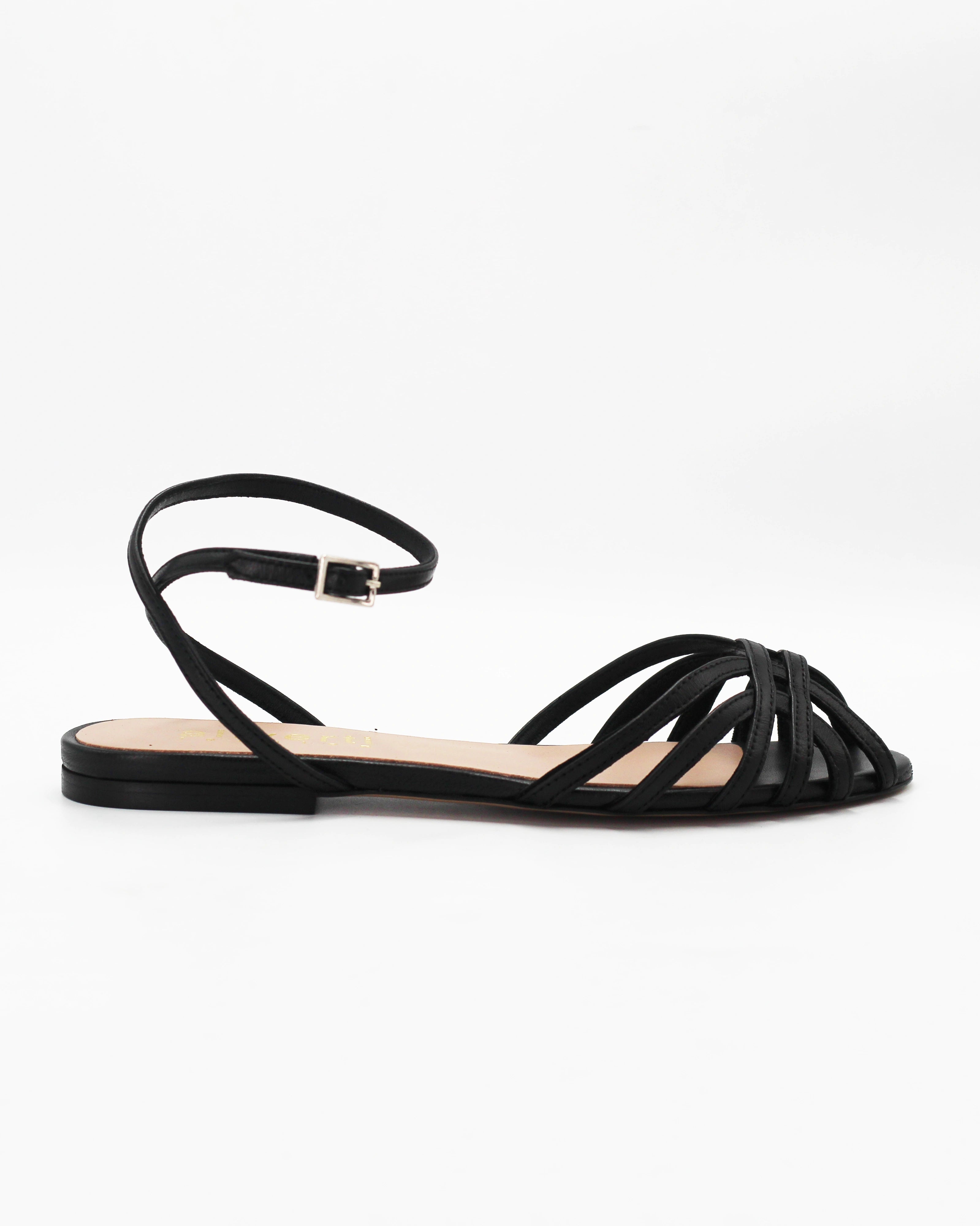 Shop the CIRA5 flat lattice sandal in black calf leather. Italian-made with a woven strap detail, adjustable ankle strap, and rubber sole. Classic summer elegance.