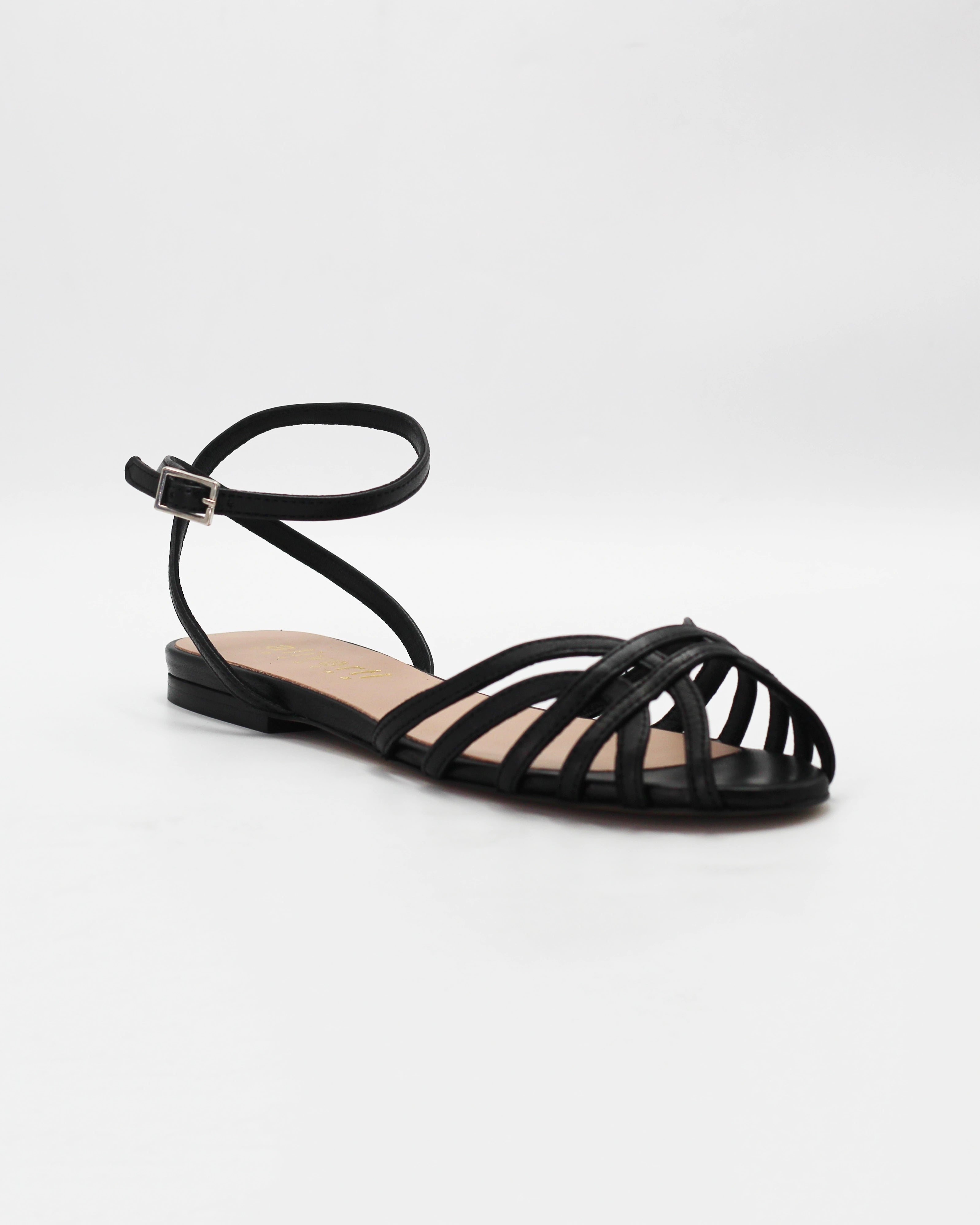 Shop the CIRA5 flat lattice sandal in black calf leather. Italian-made with a woven strap detail, adjustable ankle strap, and rubber sole. Classic summer elegance.